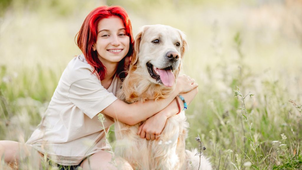 Young woman embracing golden retriever in field.