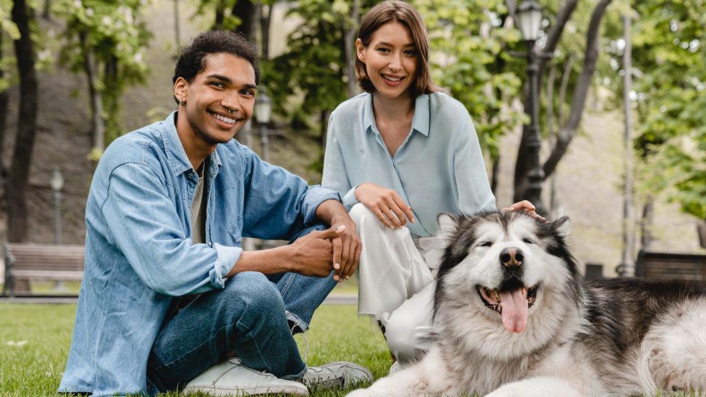 Two people with a fluffy dog in a park, representing a breed starting with 'H.'